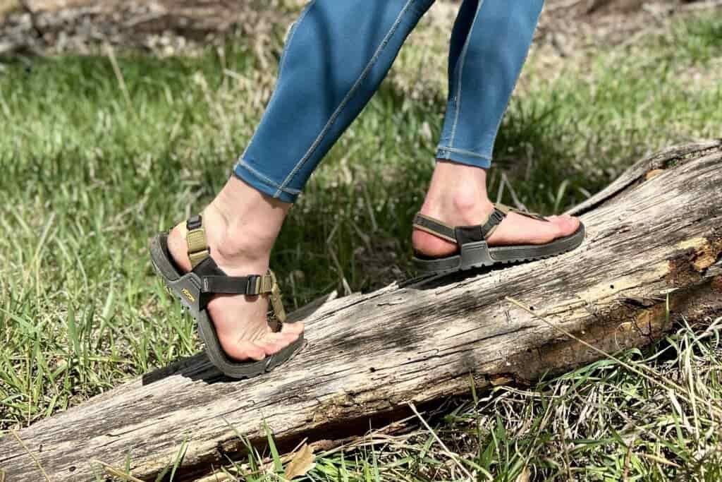 Close up image of a person in leggings wearing a pair of sandals as they balance on a log.