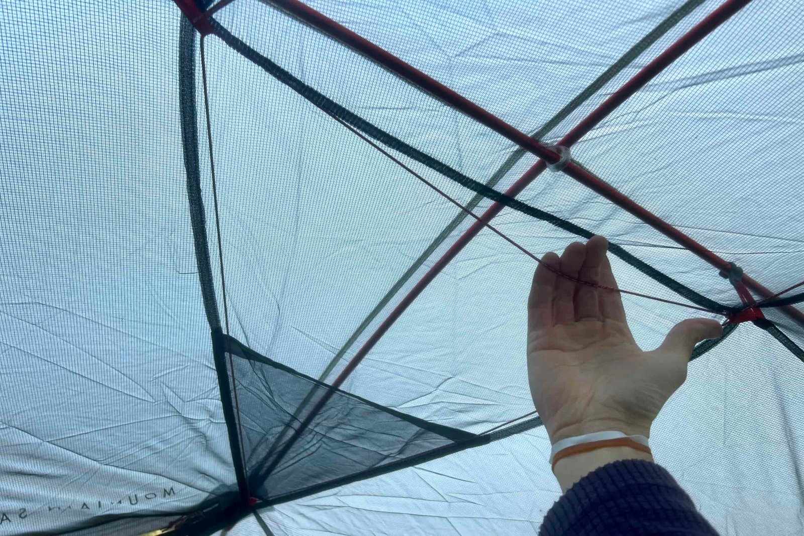 a hand reaches up to pull on a cord that is stretch across the ceiling of a tent.