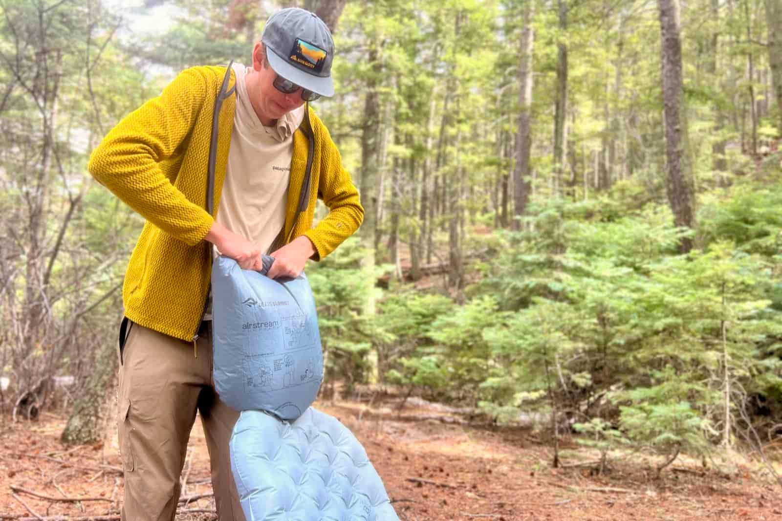 a hiker uses a pump sack to inflate a gray sleeping pad