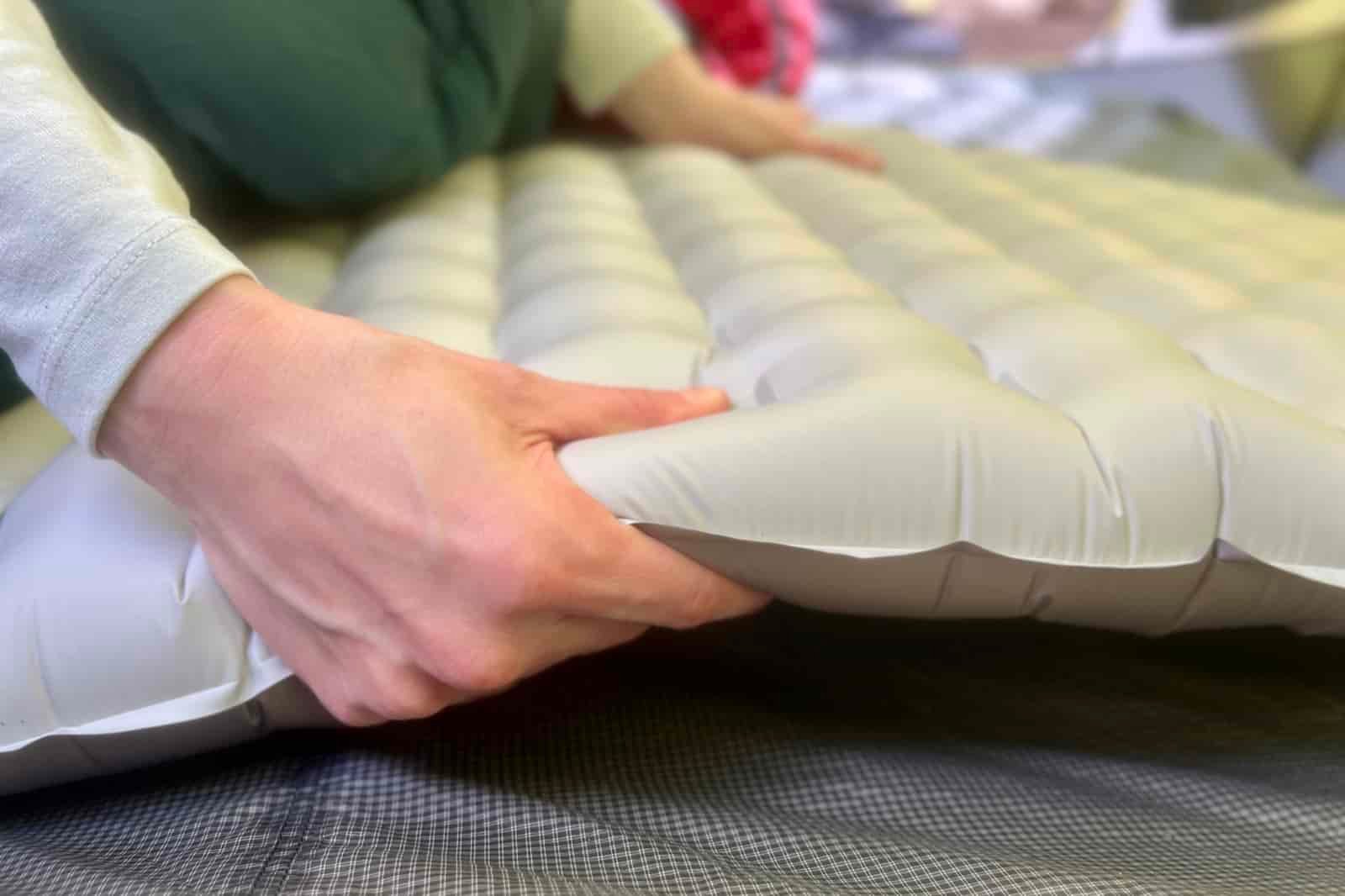a close up of a hiker grasping the thickness of a gray sleeping pad