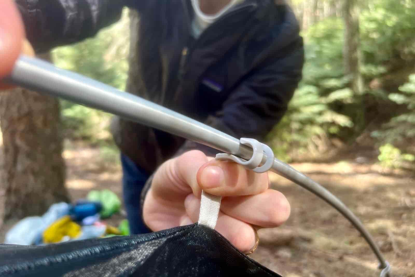 a close up of a hiker attached tent poles to the hooks on the tent body
