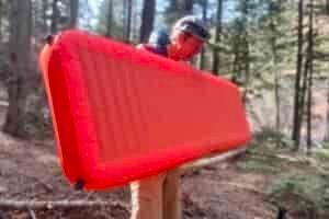 a hiker holds an inflated red sleeping pad in the middle of the woods