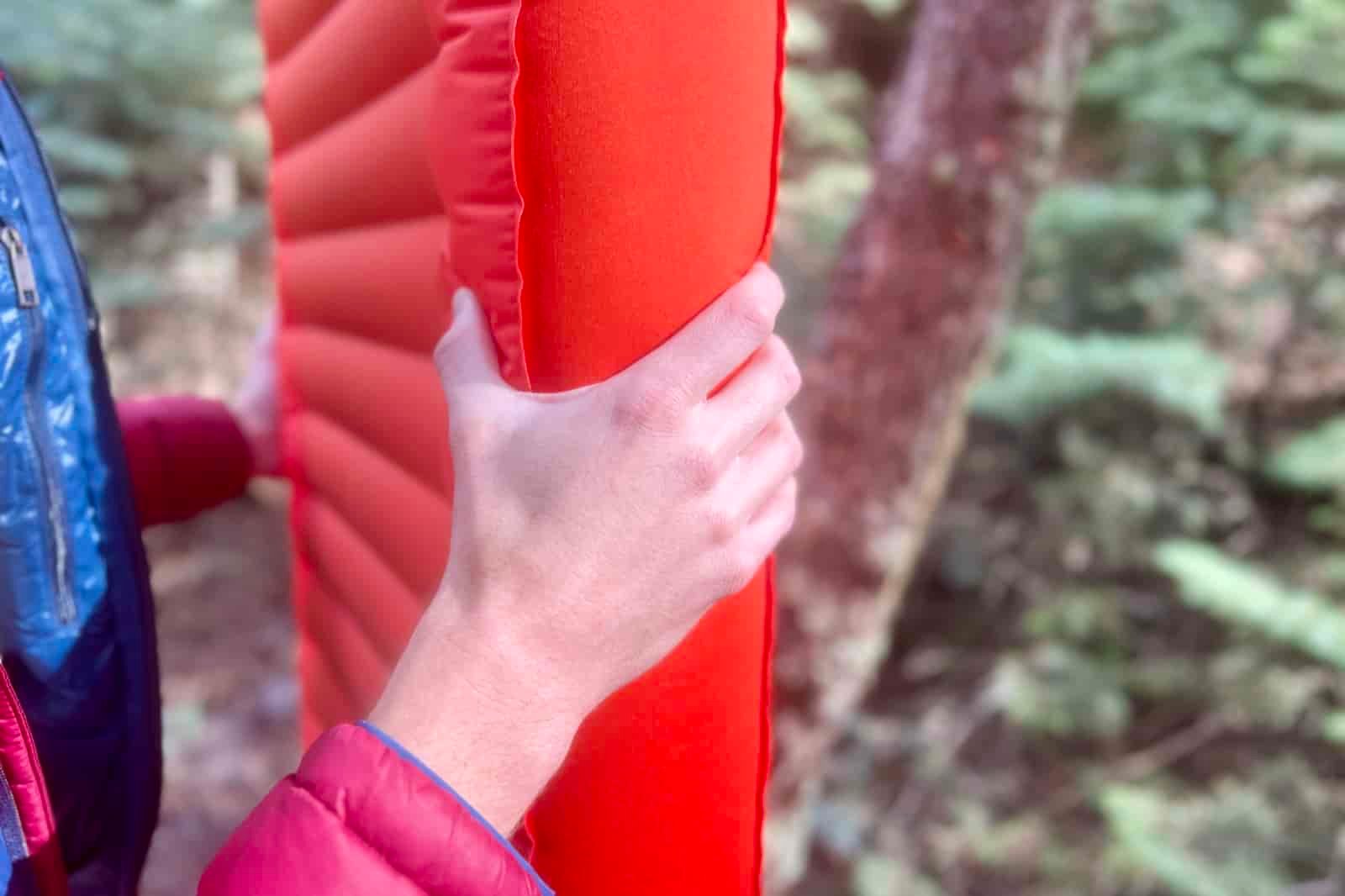 a closeup of a hand grasping the thickness of a sleeping pad