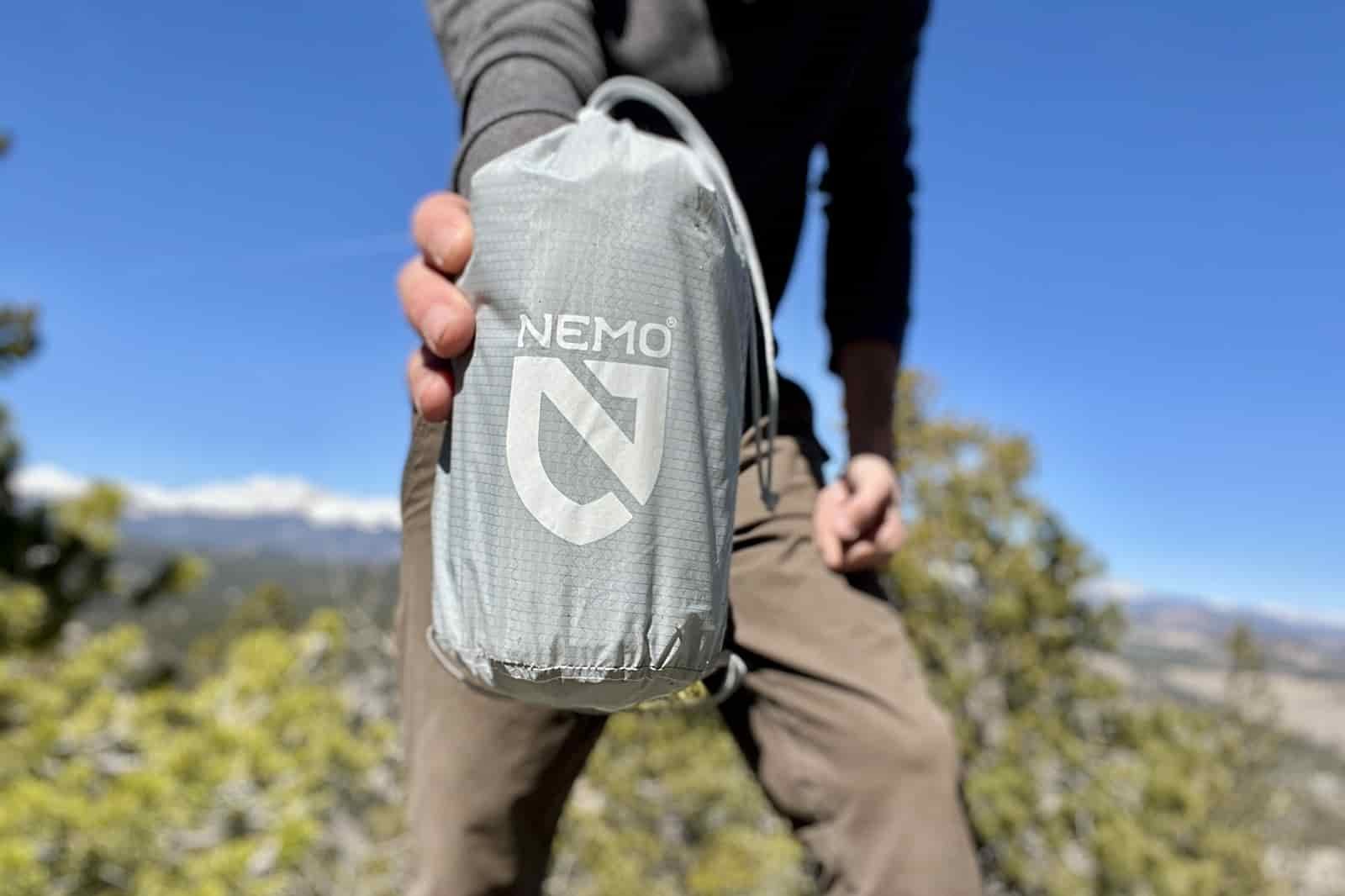 a hiker holds a gray stuff sack containing a sleeping pad