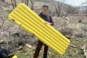 a hiker holds a yellow sleeping pad in a forest