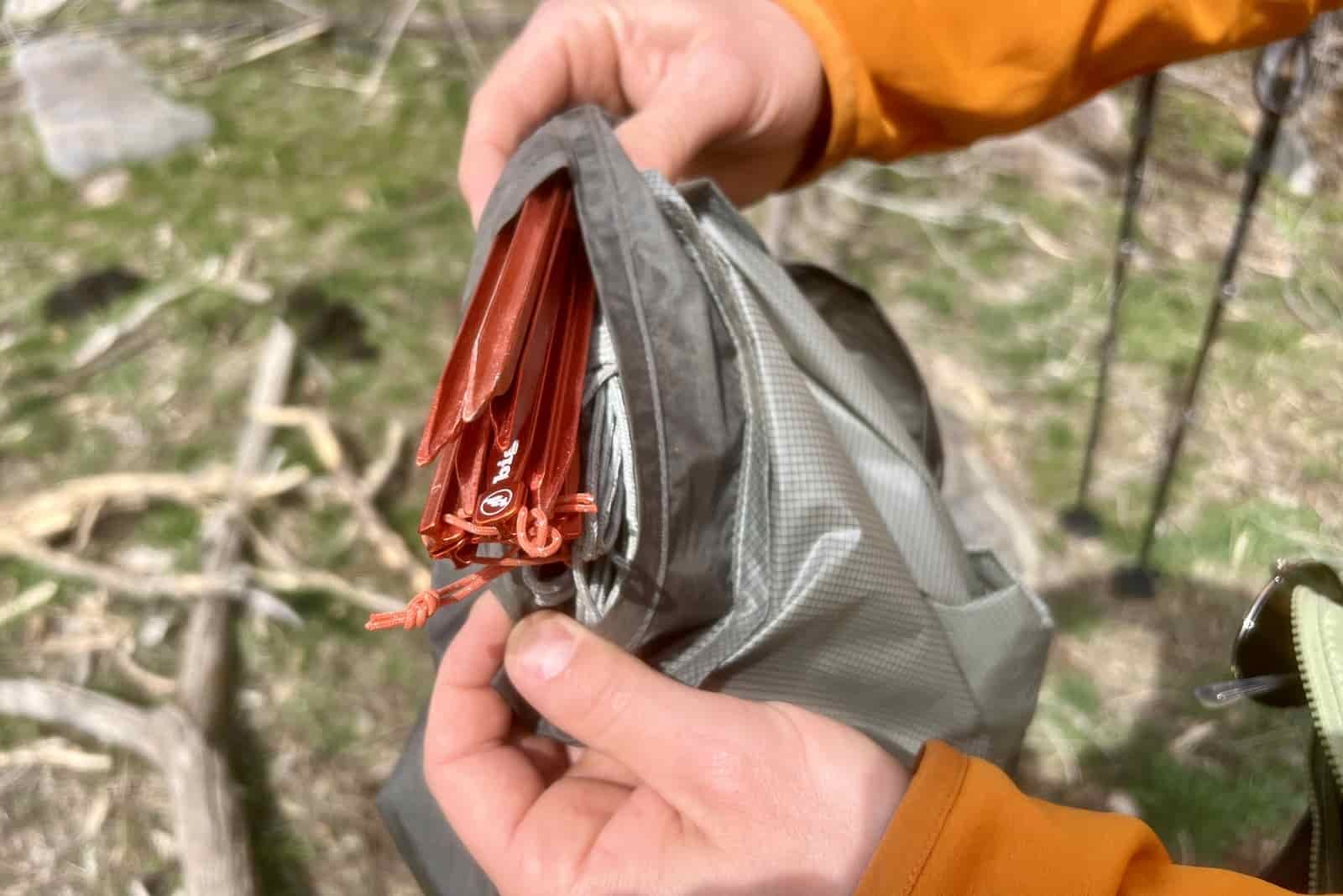 a close up of hands showing stakes in a secret pocket in a tent stuff sack