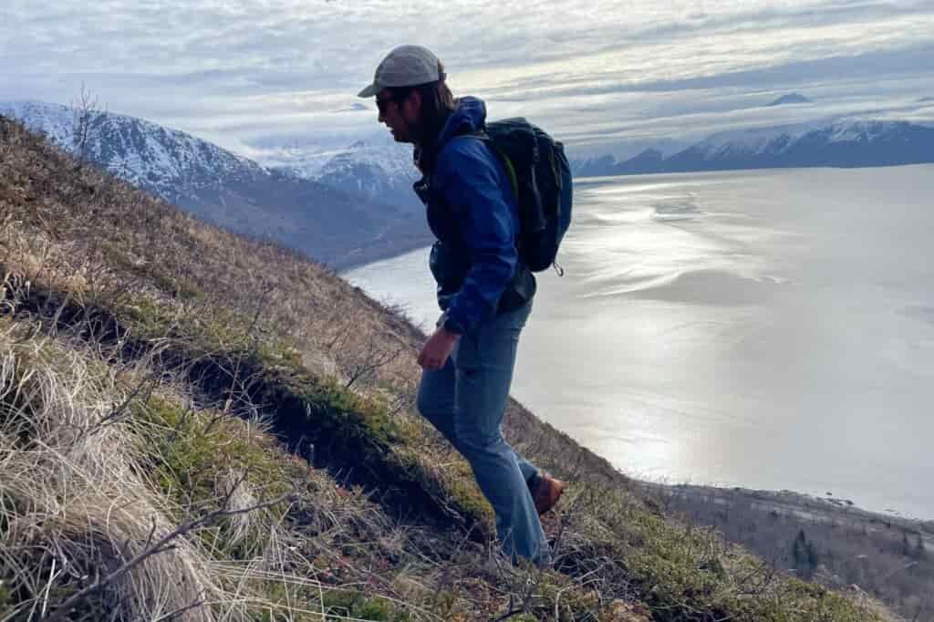 A man hikes up a trail with mountains in the background.