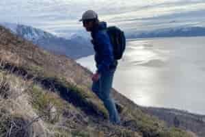 A man hikes up a trail with mountains in the background.
