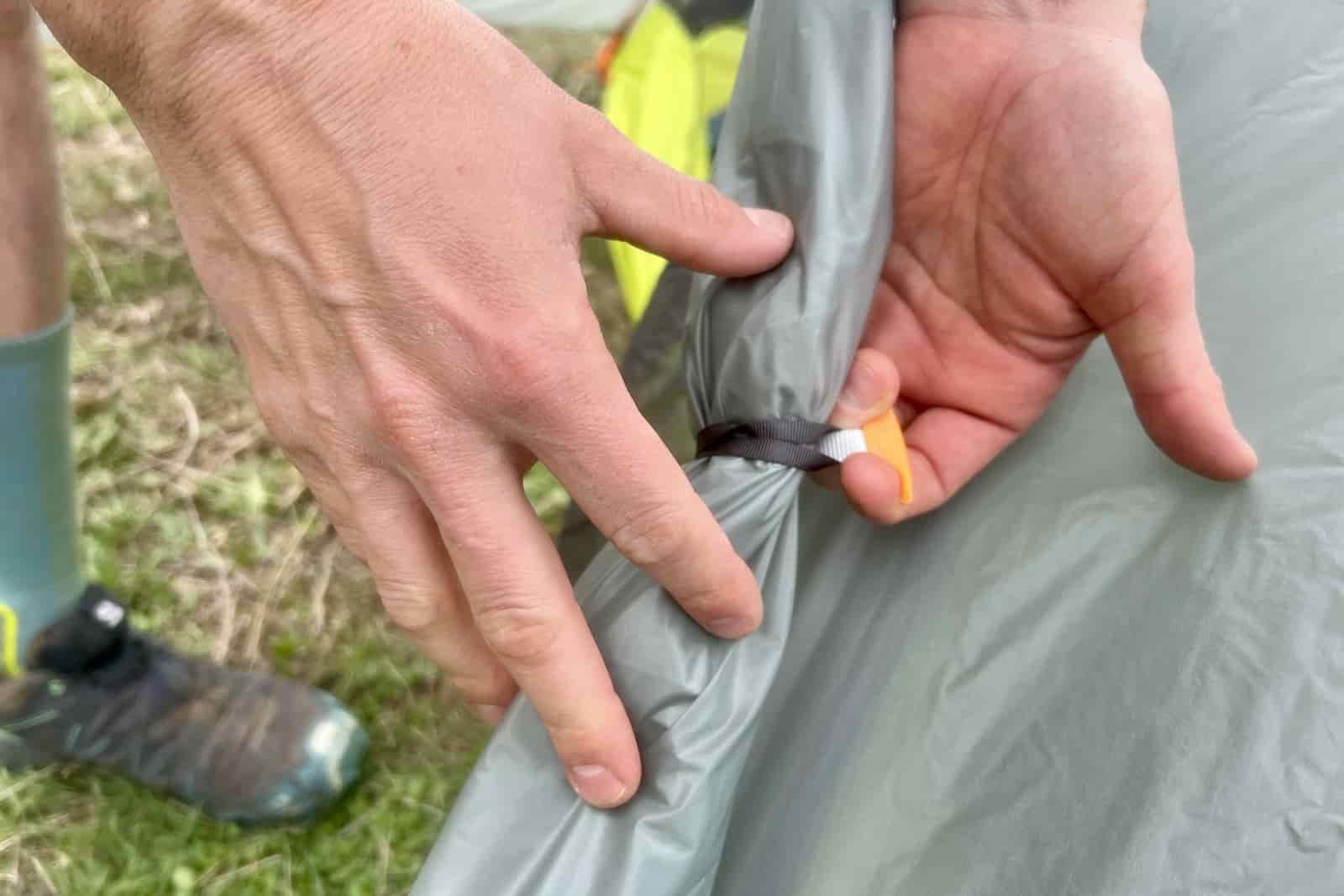 a close up of a hiker holding the door tie back of a tent