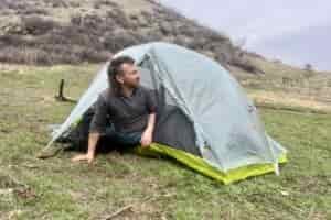 a hiker leans out of a light grey tent