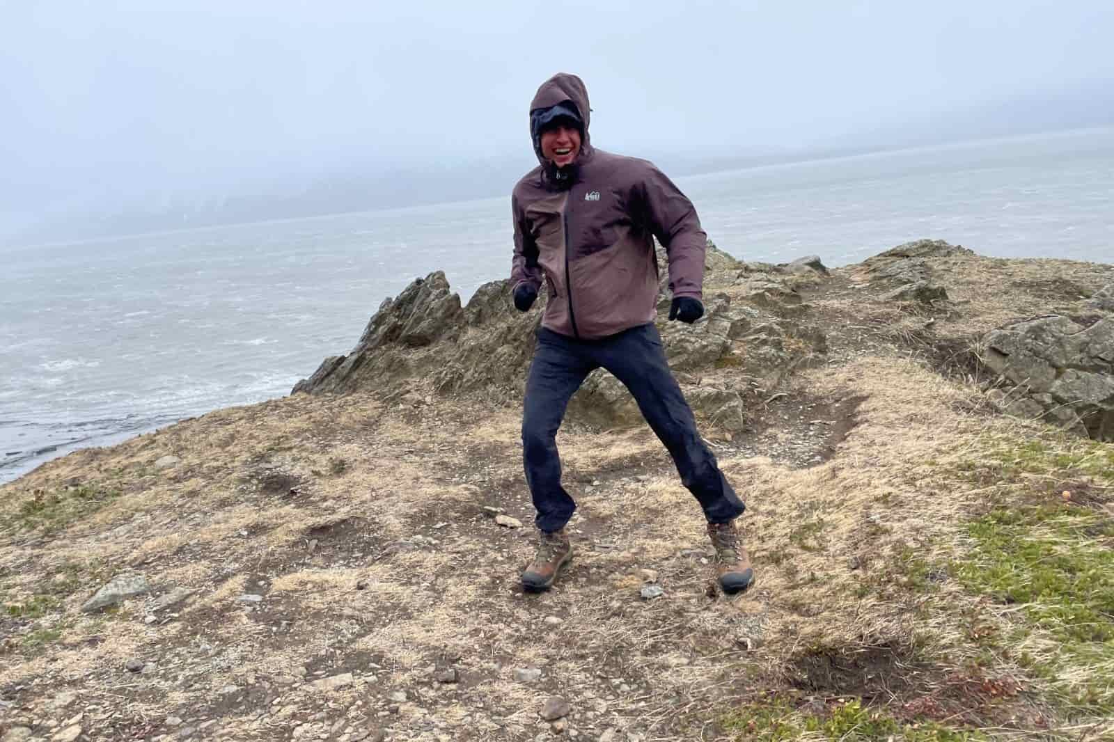 A man stands on a point above an ocean and mountain background.