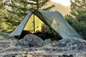 a hiker lounges in a green trekking pole tent at sunset