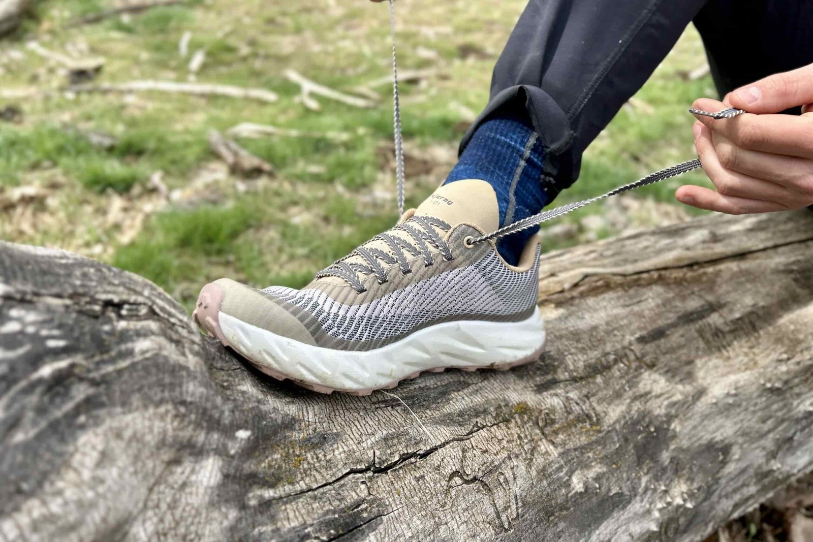 Close up image of a person tying the shoelaces on a pair of trail runners while sitting on a log.