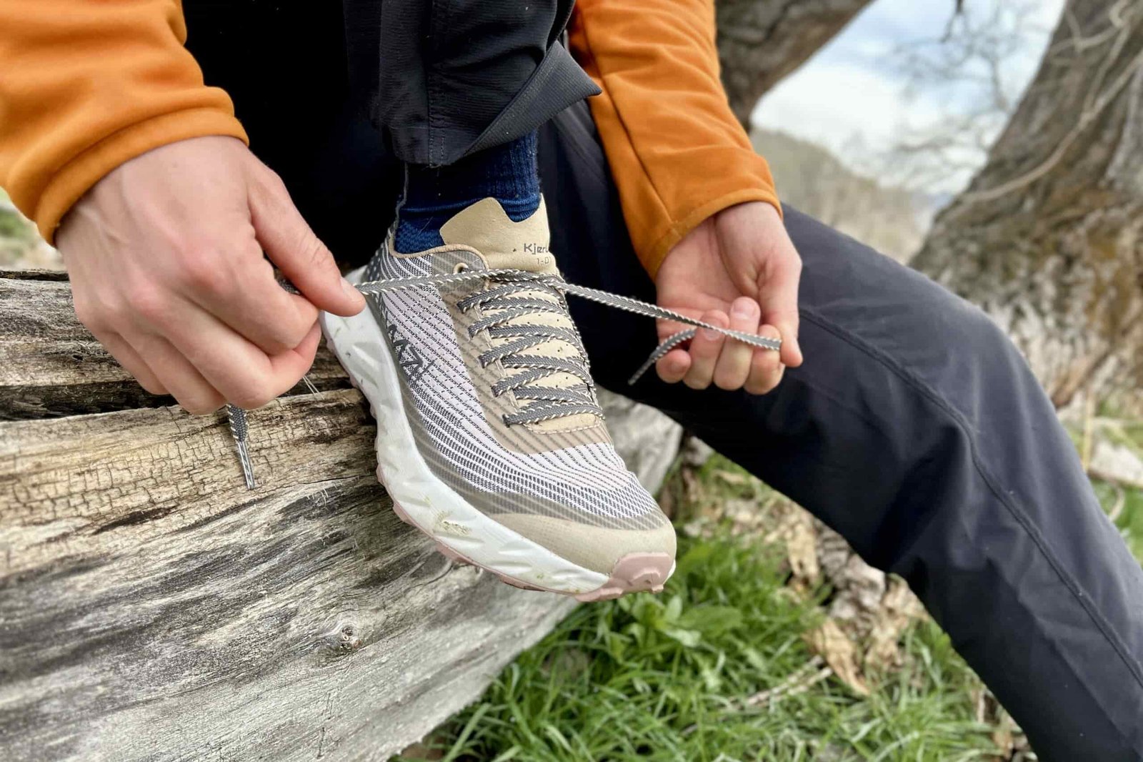 Close up of a person tying a pair of trail running shoes while sitting on a log