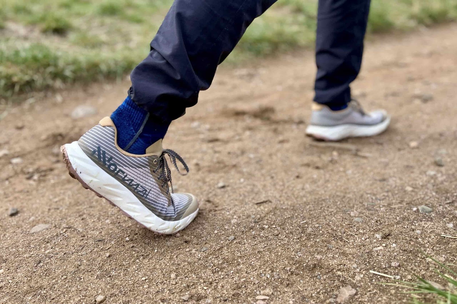 Close up from the side of a person walking in a pair of trail runners on a dirt path.