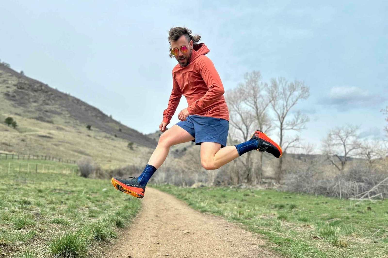 A man in running attire jumps in the air in a hilly setting.
