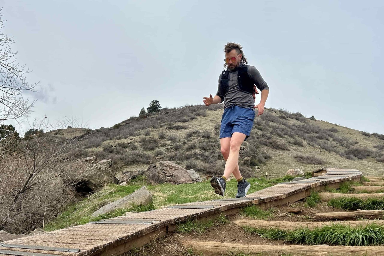 A man runs down a wooden board on a trail in a hilly wilderness setting.