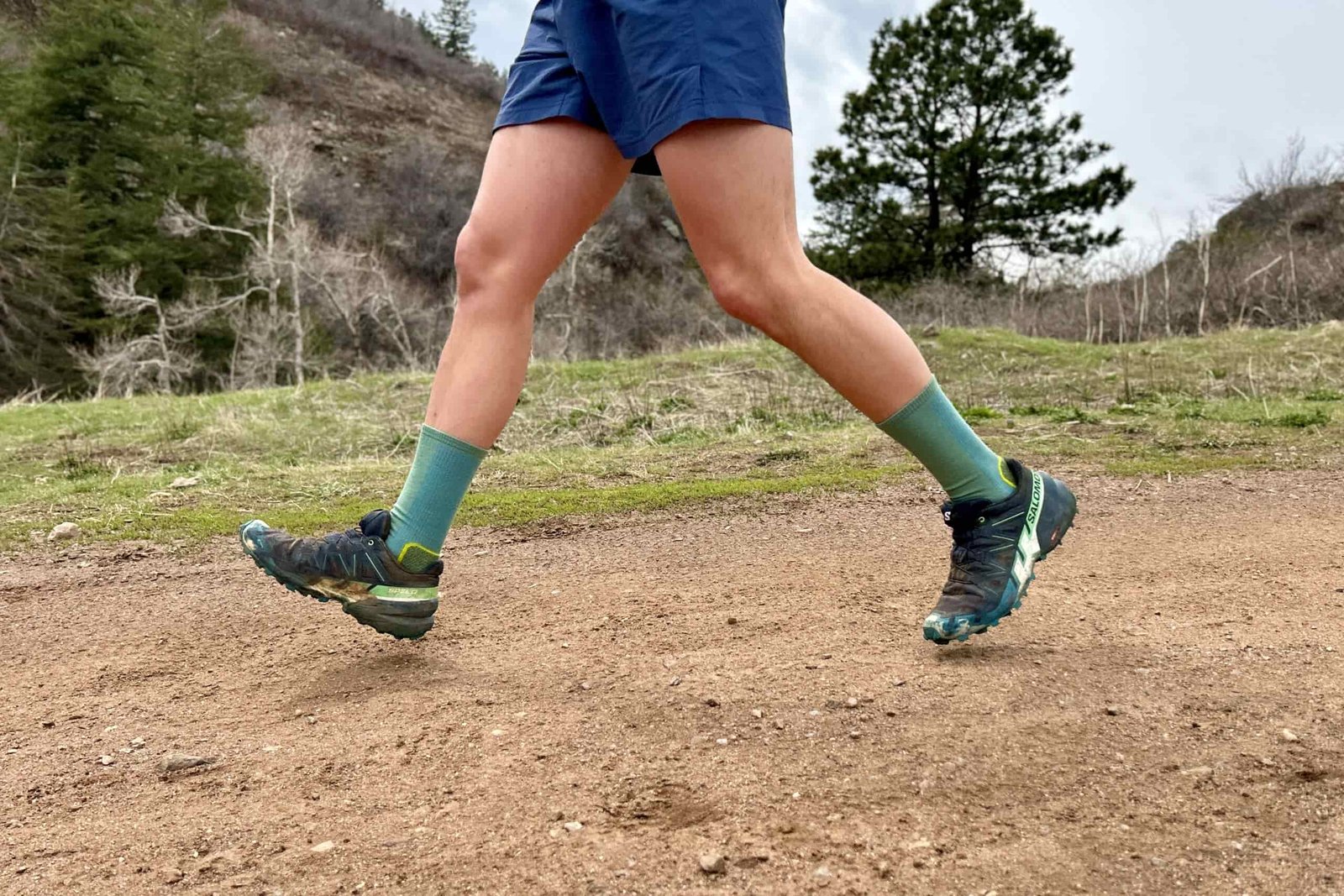 Side-view of a runner wearing shorts and trail runners as they jog down a trail