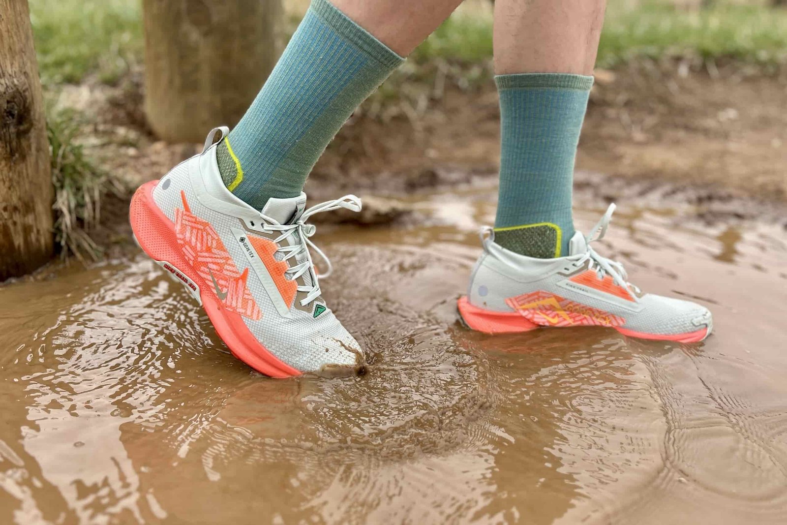 A person walks through a puddle of muddy water in a pair of white trail runners.