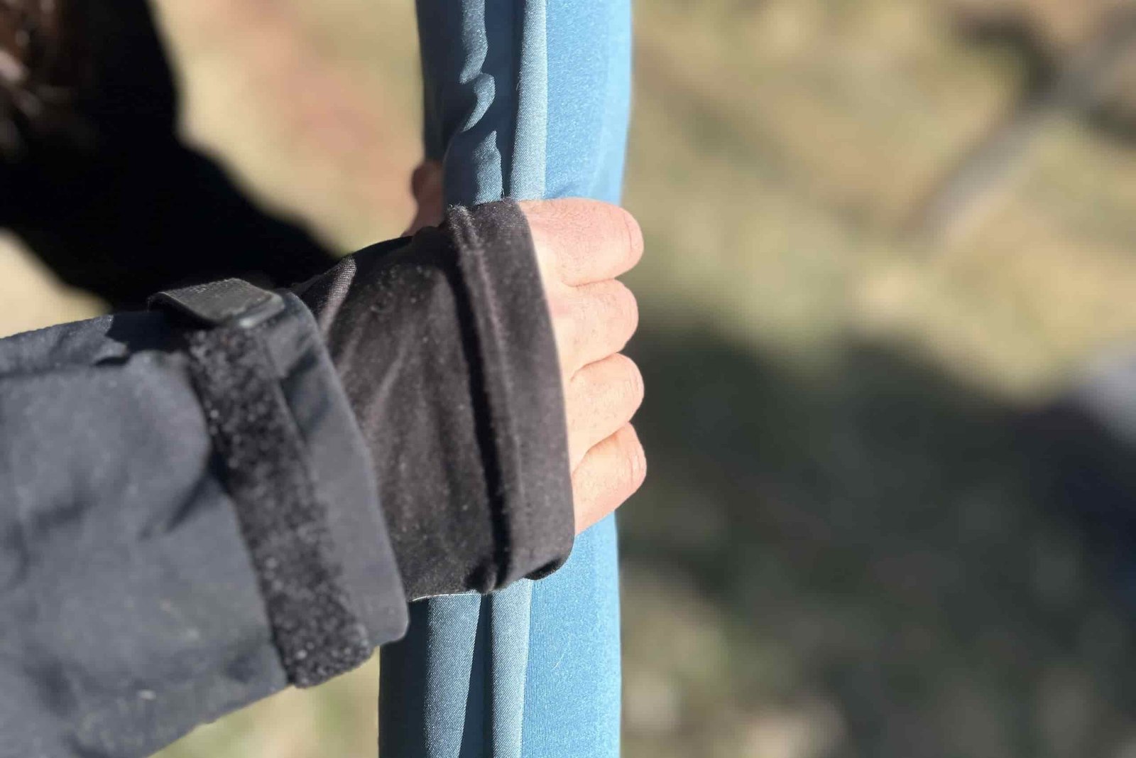 A person's hand holds the side of a thin sleeping mattress.