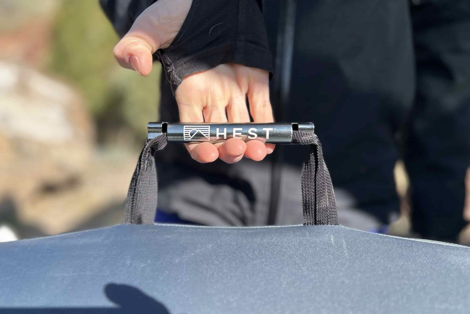 Close up image of a person's hand holding the thick nylon and metal handle of a camping mattress with the product label, HEST, prominently displayed.