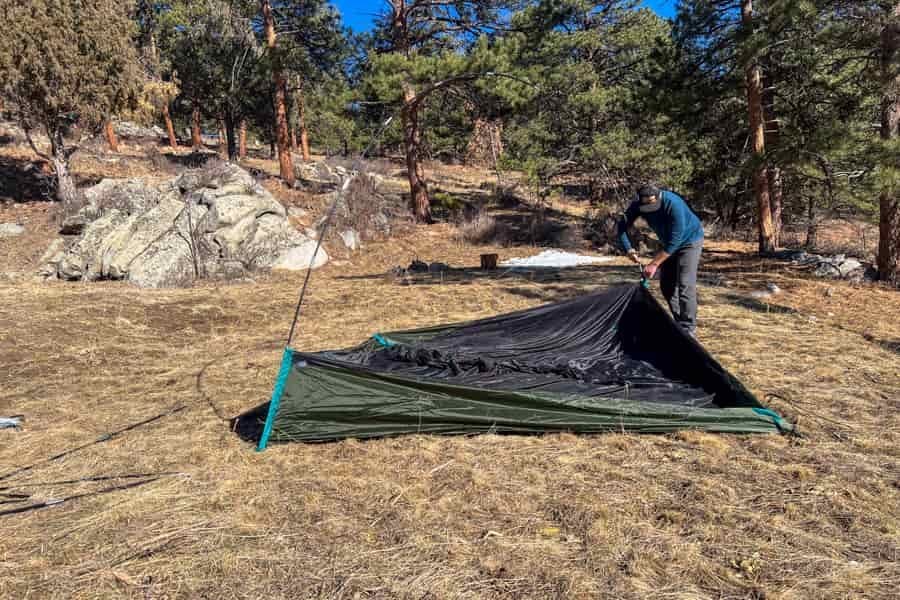a man in a filed of brown grass begins to set up a tent.