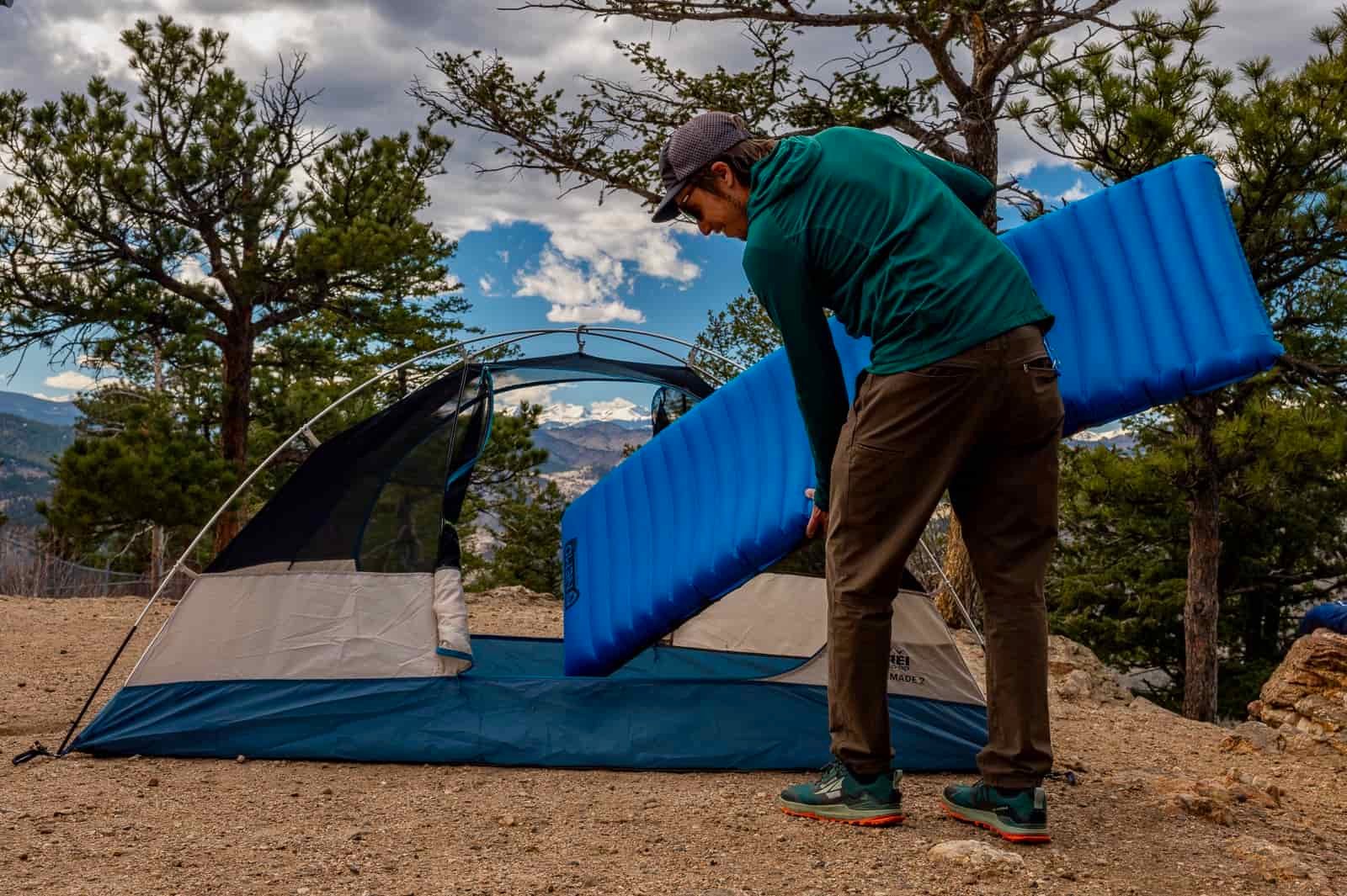 a hiker slides a blue inflatable sleeping pad into a tent