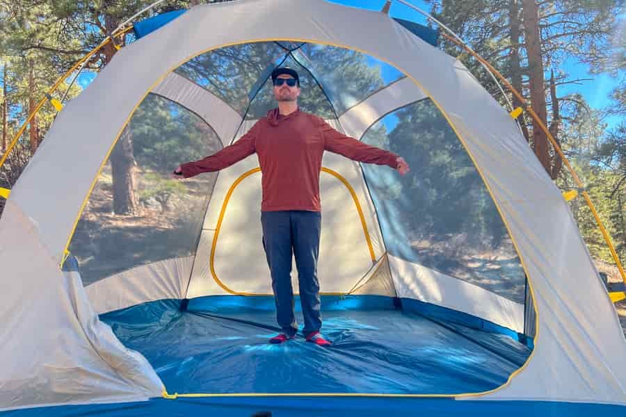 A man standing with his arms out inside an empty tent.