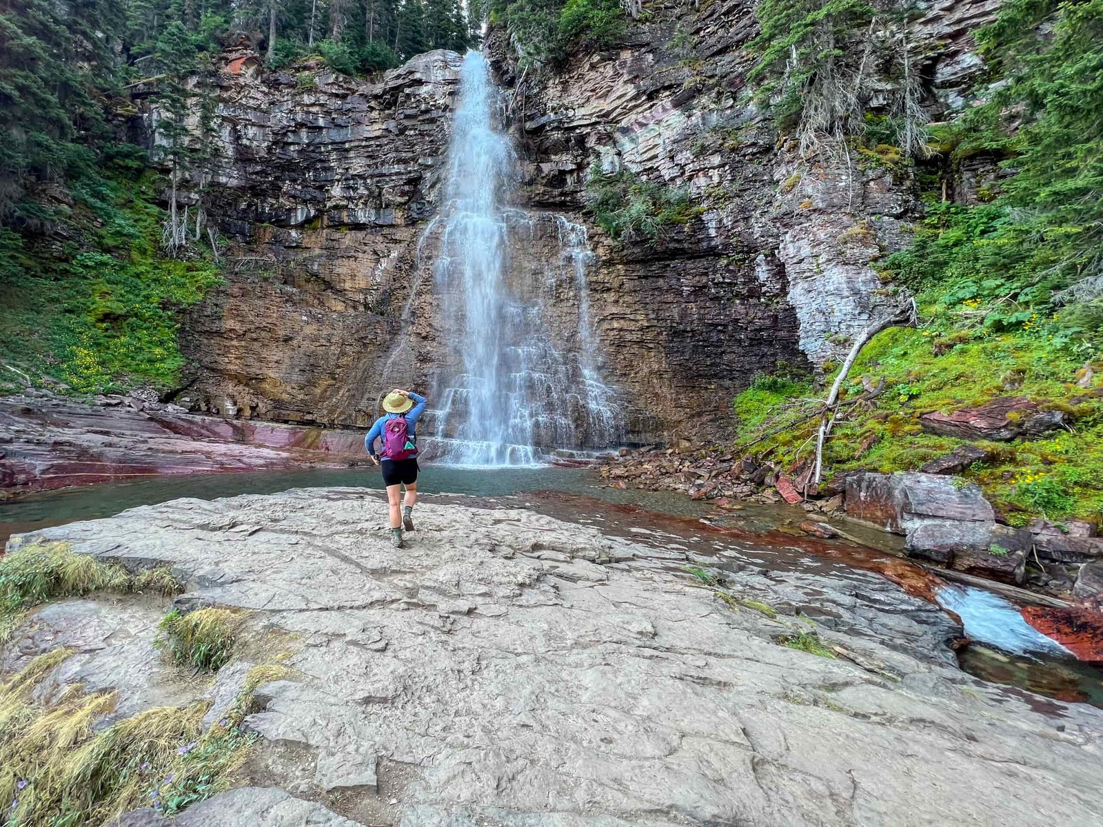 a women walks toward a tall waterfall