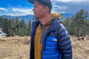 a man in a blue jacket standing in a field. He's facing somewhat away from the camera and lookign off into the distance.