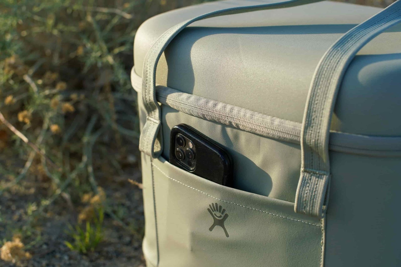 A close up of a cell phone poking out of the front pocket of the Hydro Flask Carry Out cooler.