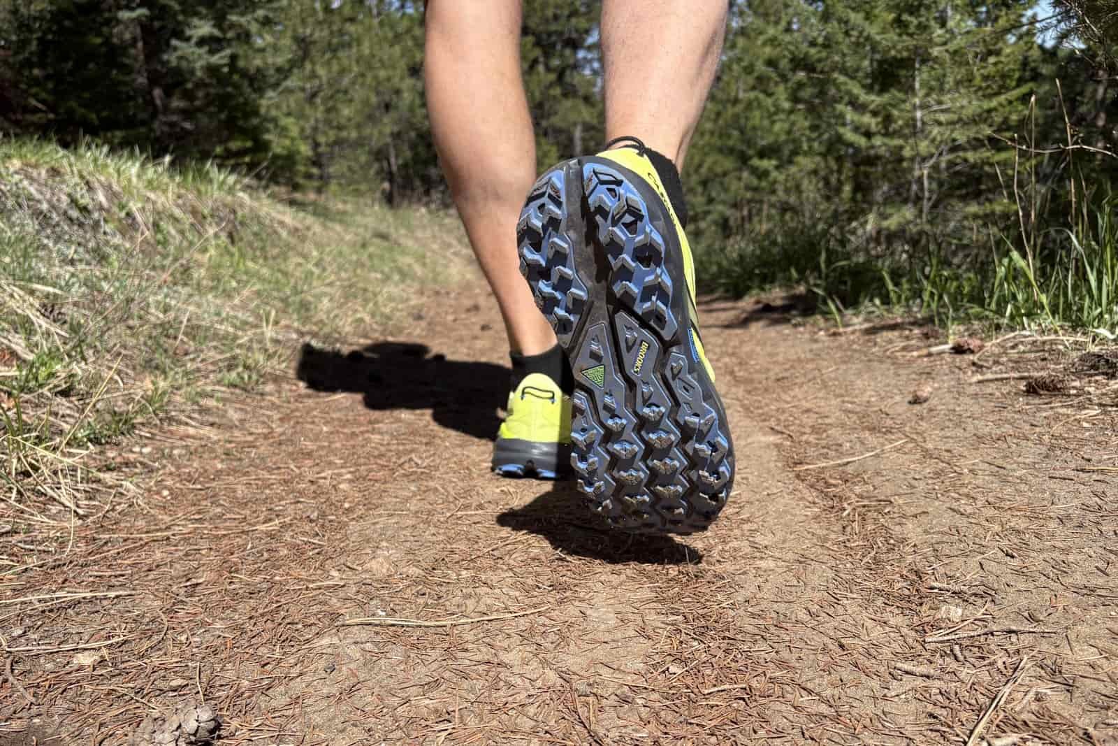The feet of a man waking on a hiking trail with the underside of his right foot showing the shoe's traction.