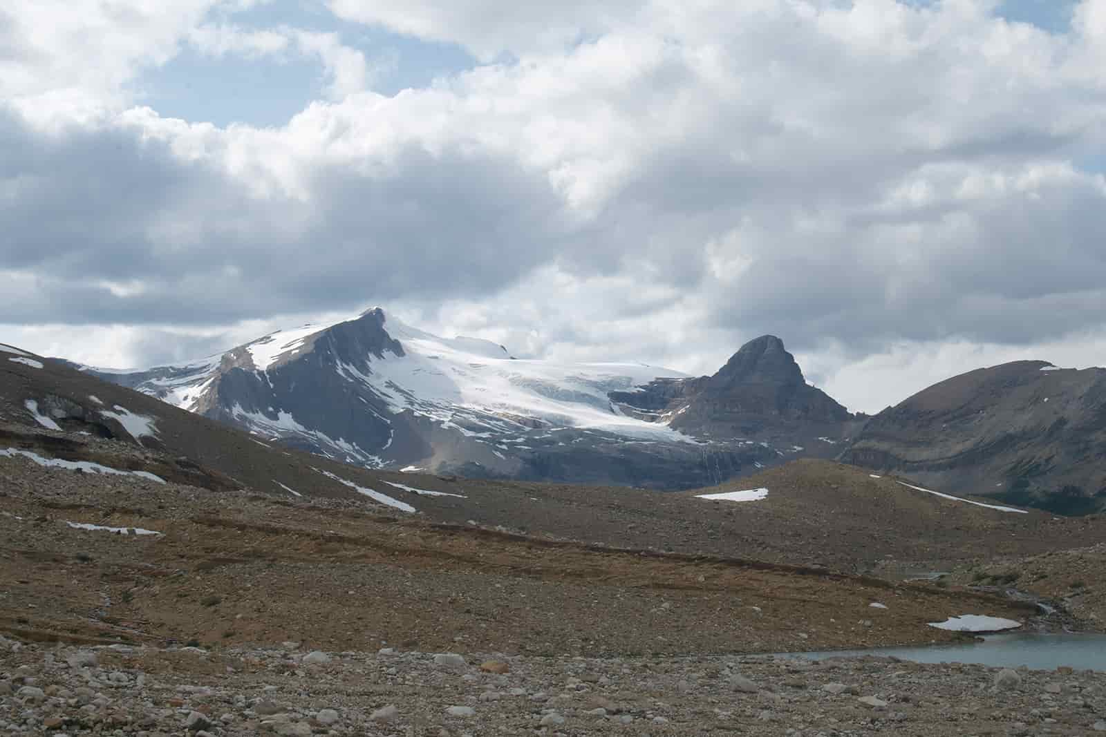 The viewer is standing in a rocky, open area. There is a mountain rising in the distance covered in a glacier.