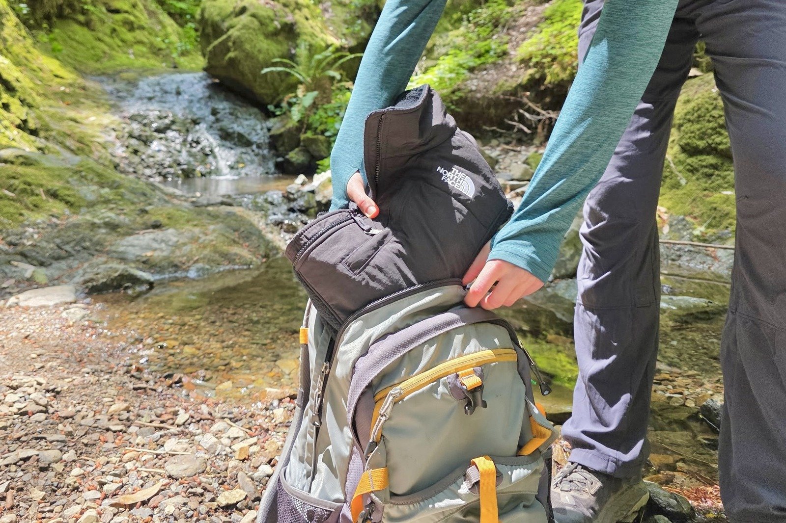 Woman stows away her folded fleece jacket in her day pack.