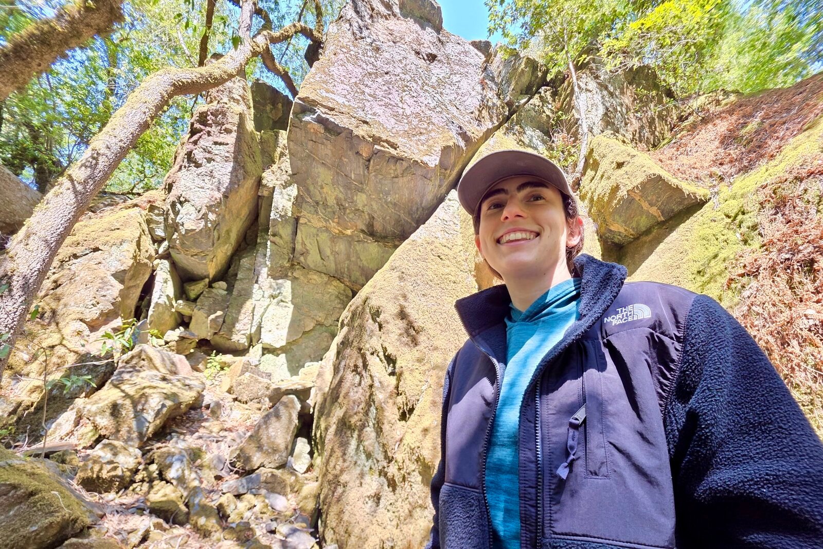 Woman stand before a rock outcropping, modeling the chest of the North Face fleece.