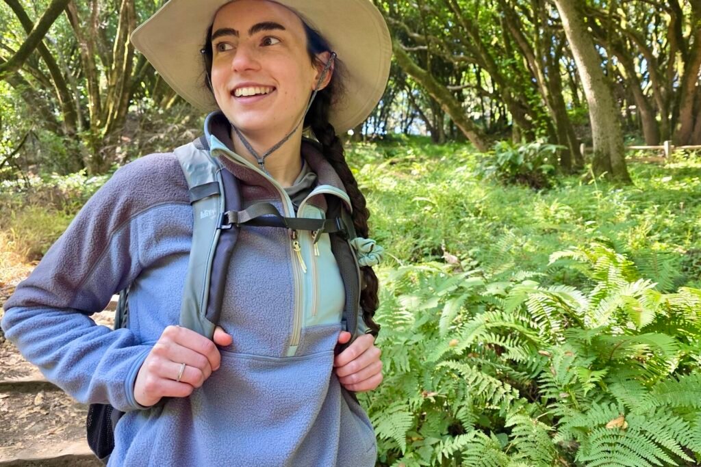 Woman stands on a trail wearing a backpack over her fleece jacket.