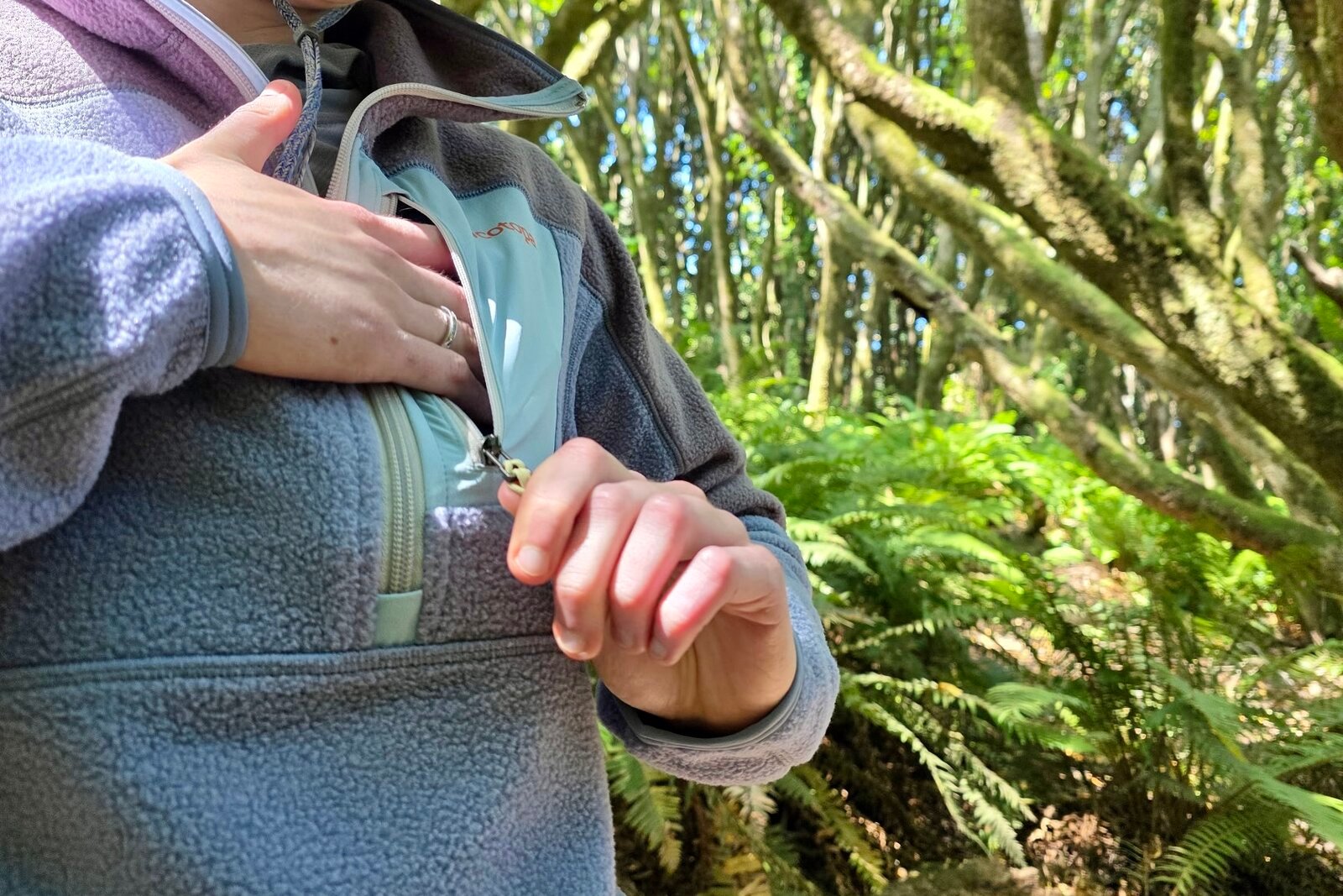 A woman displays the chest zippered pocket in front of her fleece jacket.