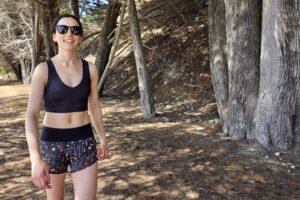 A woman walks through a forest in her sports bra and Oiselle shorts.