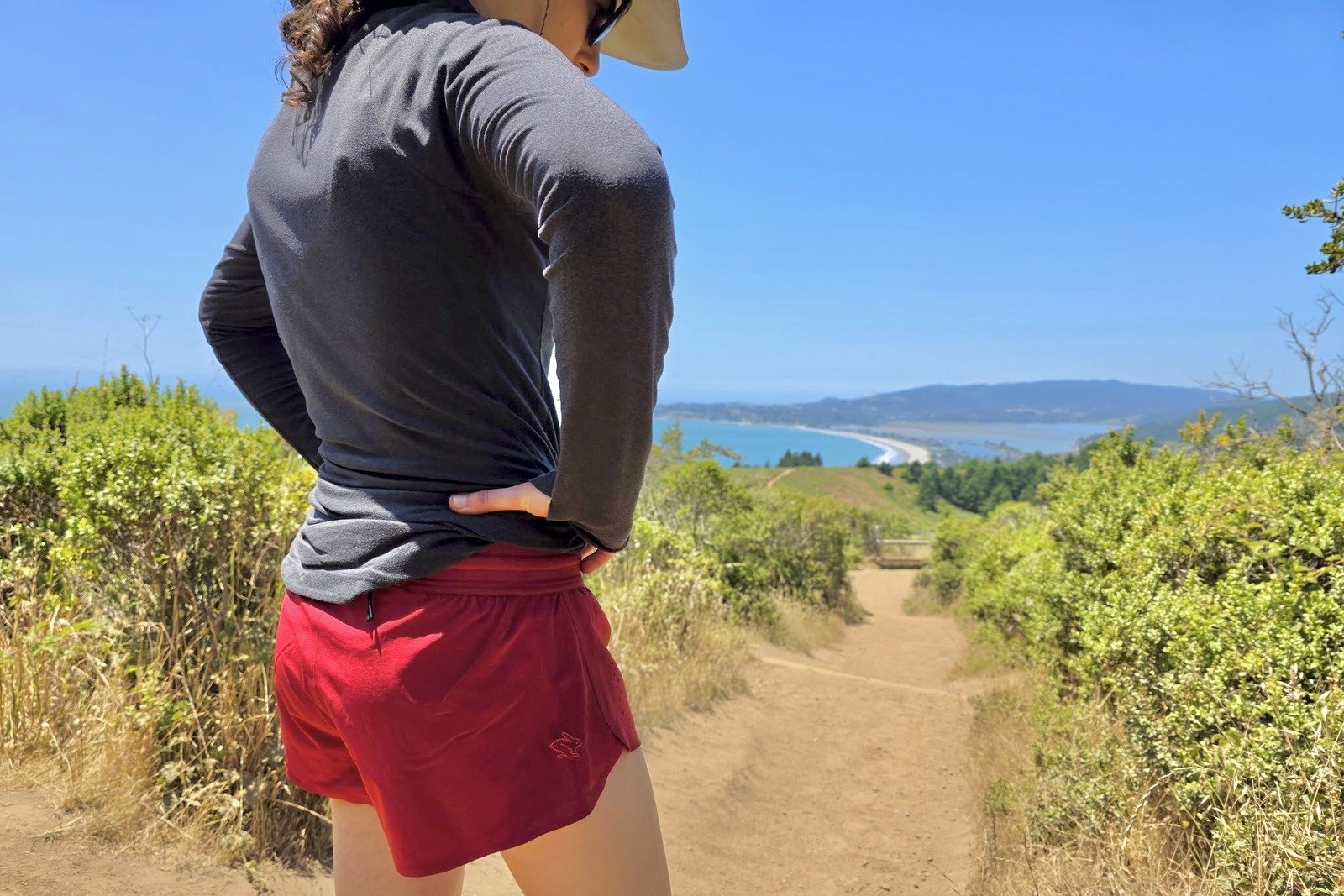 A woman stands in the middle of the trail with a view of the Pacific Ocean.
