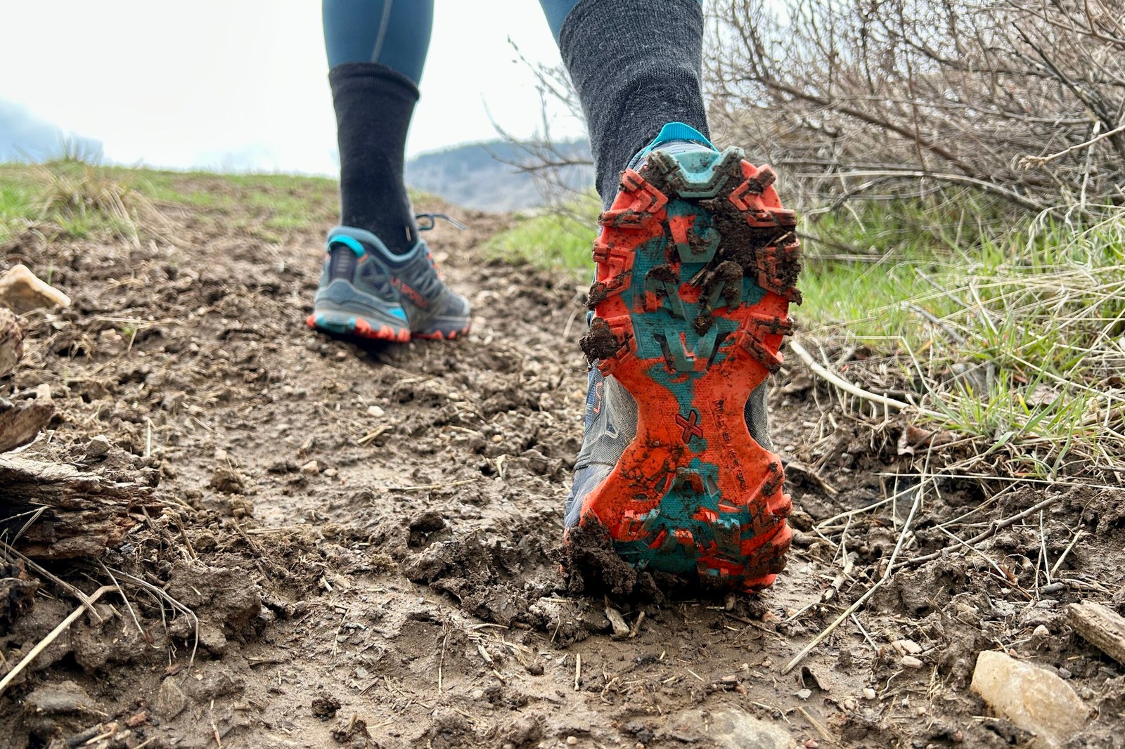 Underside traction view of a trail runner in a muddy section of trail.