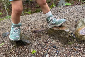 Child hiking over wet rocks on a forest trail while wearing Adidas Terrex AX4R Mid shoes.