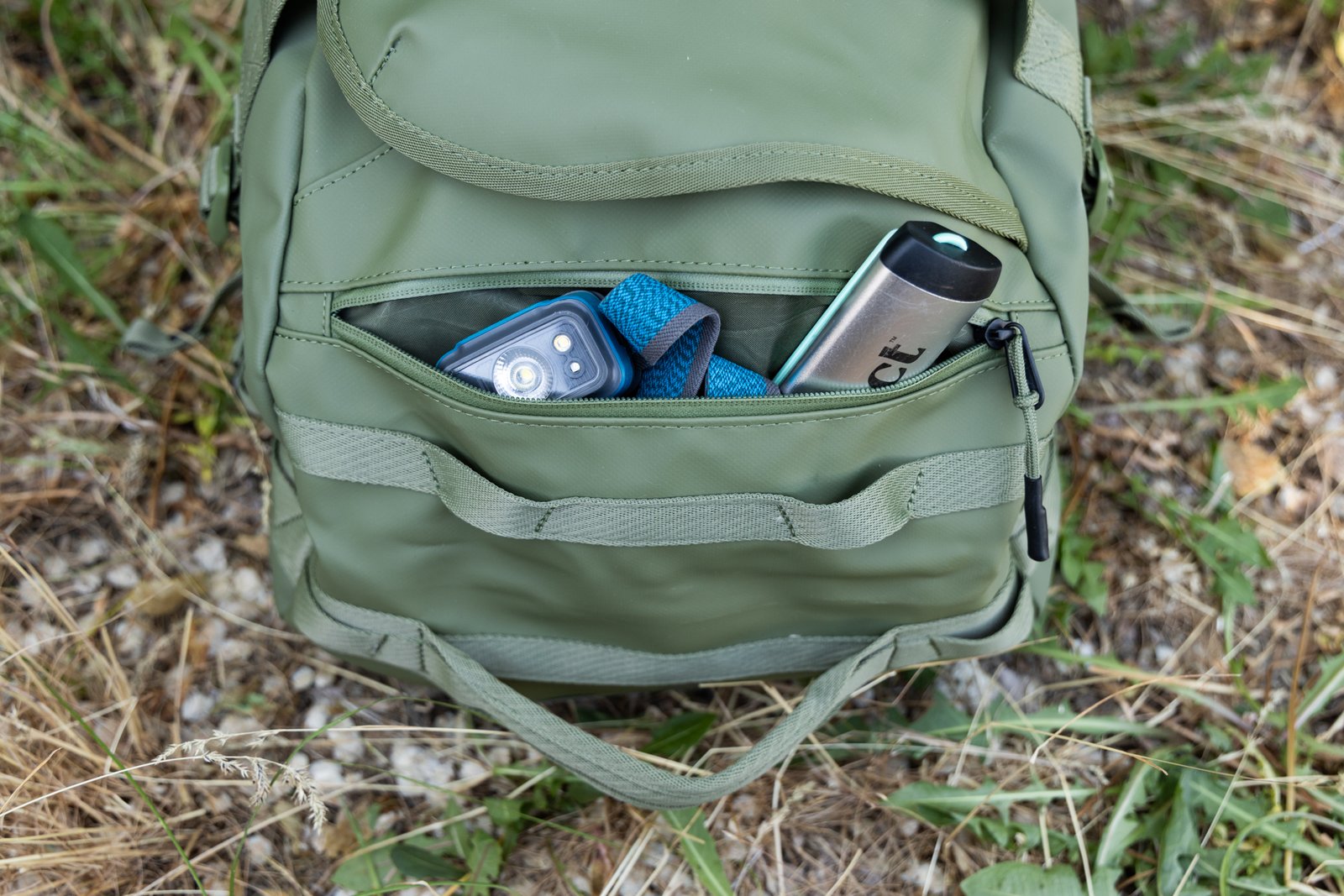 Small items like a cathole shovel and headlamp peak out of the exterior zipper pocket on the end of the Thule Chasm duffel.