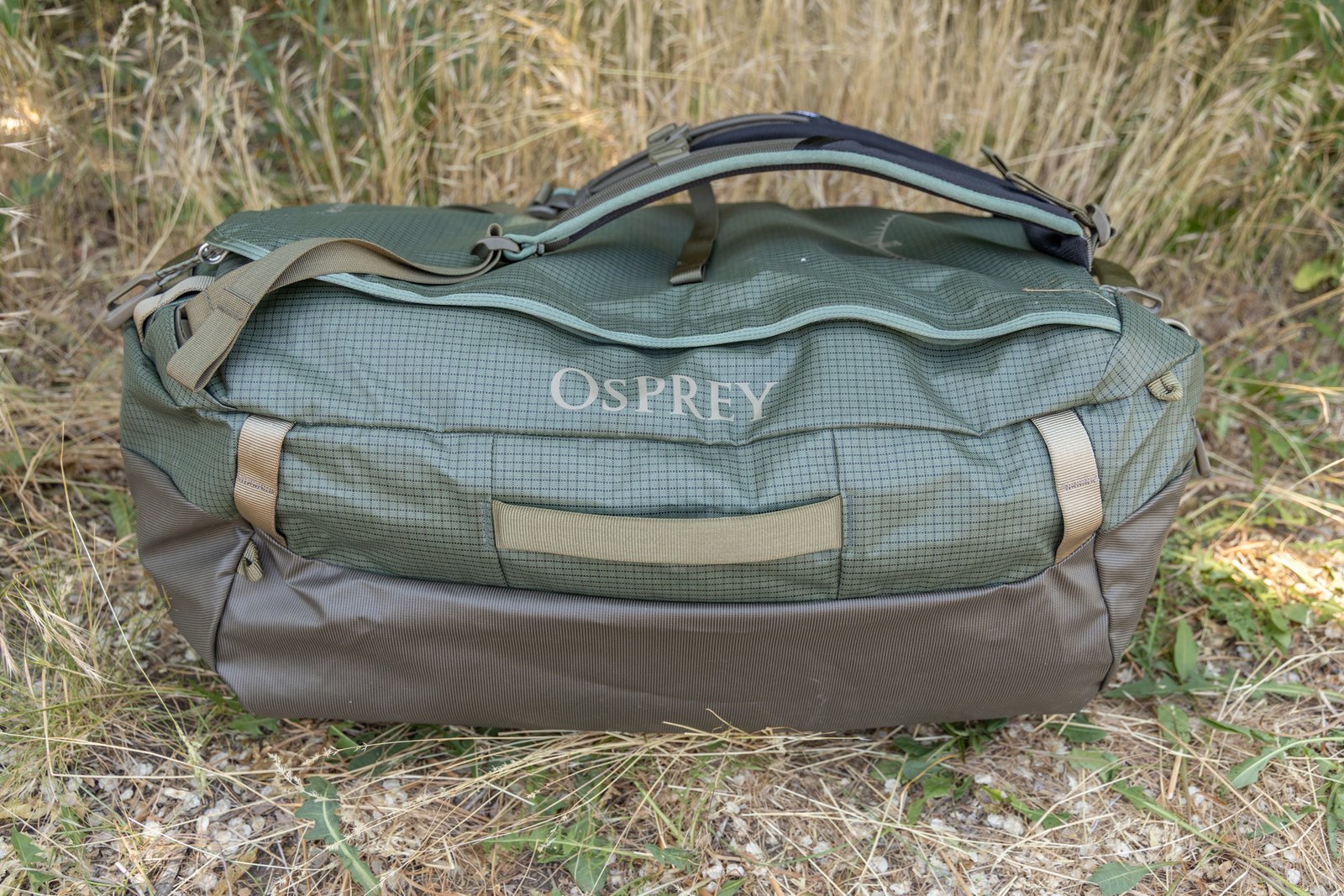 A side view of the Osprey Transporter duffel shows durable materials, heavy duty cargo handles on the side, webbing loops, and backpack straps attached atop the lid.