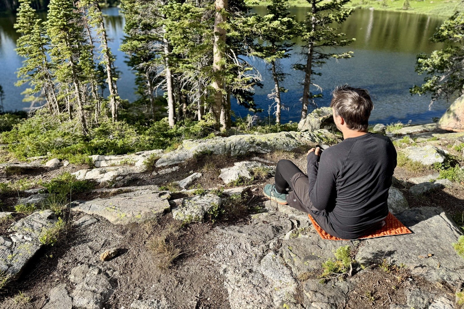 a hiker sits on a rock looking away from the camera towards an alpine lake