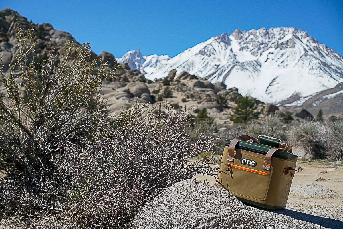 The RTIC Soft Pack leans on top of a rock with boulders and a mountain in the distance.