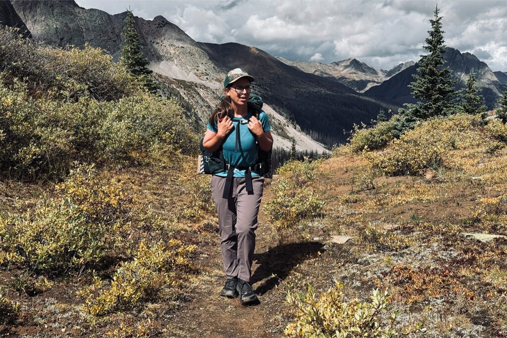 A person wearing the Dynama pants is wearing a backpacking and walking on a trail in the mountains.