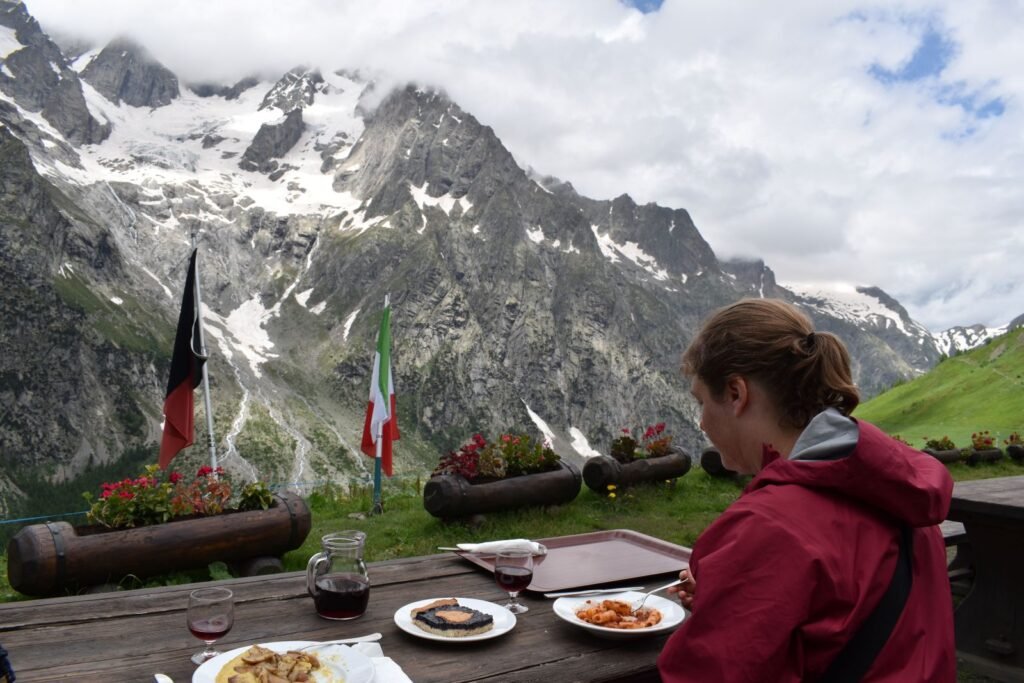 A female hiker eats rigatoni and drinks red wine with Mount Blanc in the background