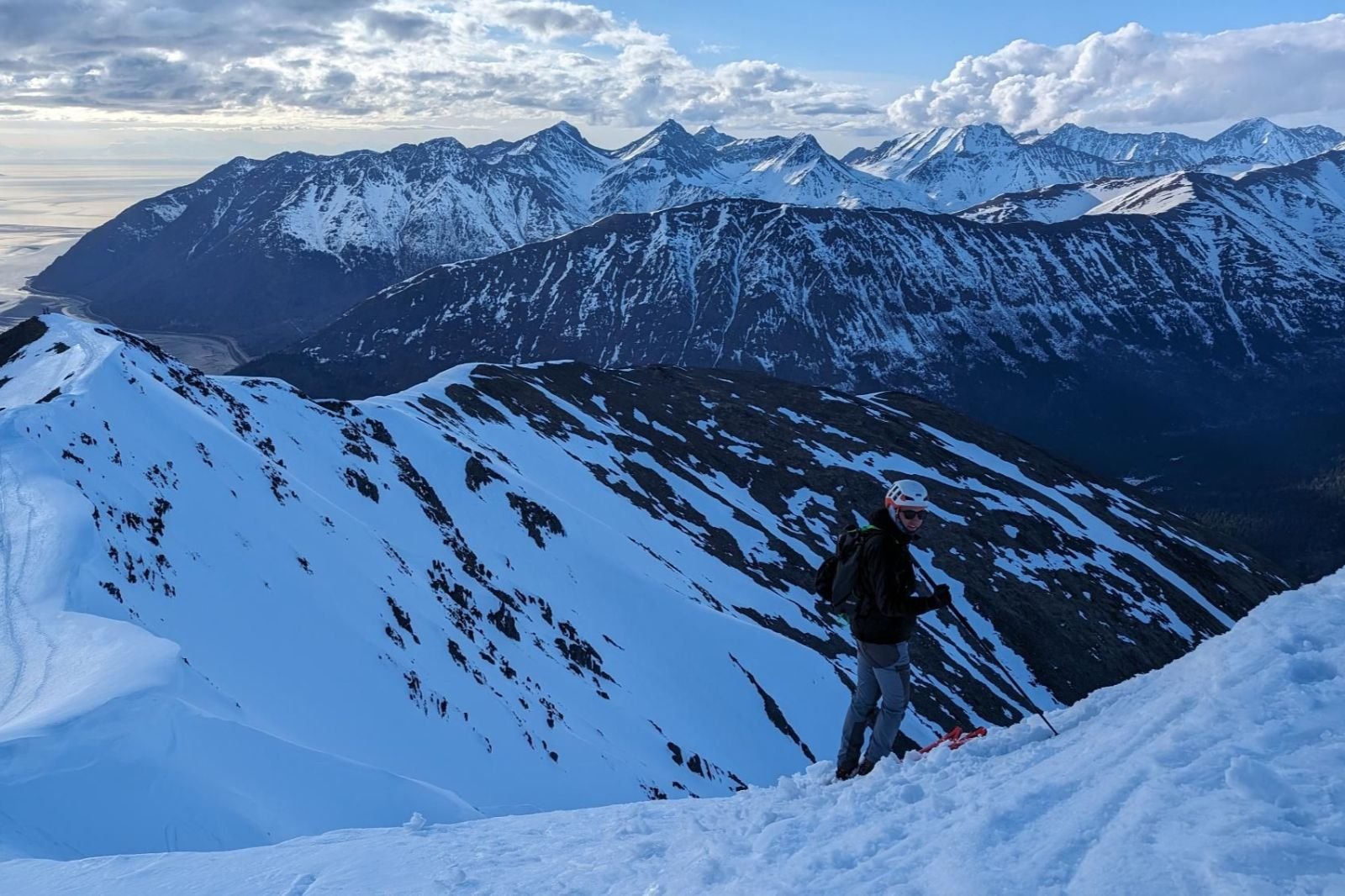 A man skis on a ridgeline above mountains and ocean.