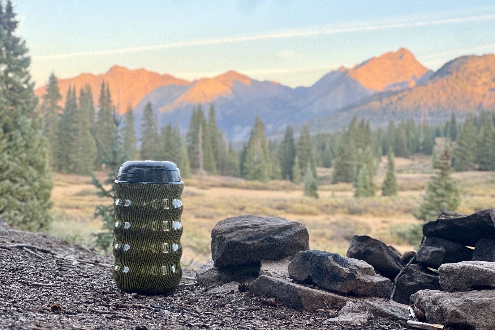 a bear canister sits next to a fire ring with mountains in the background
