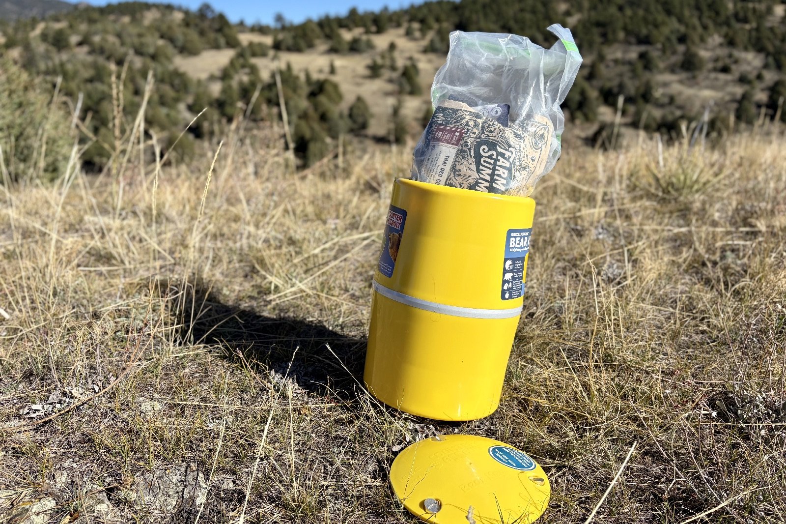 a yellow bear canister sits in the grass with a food bag sticking out